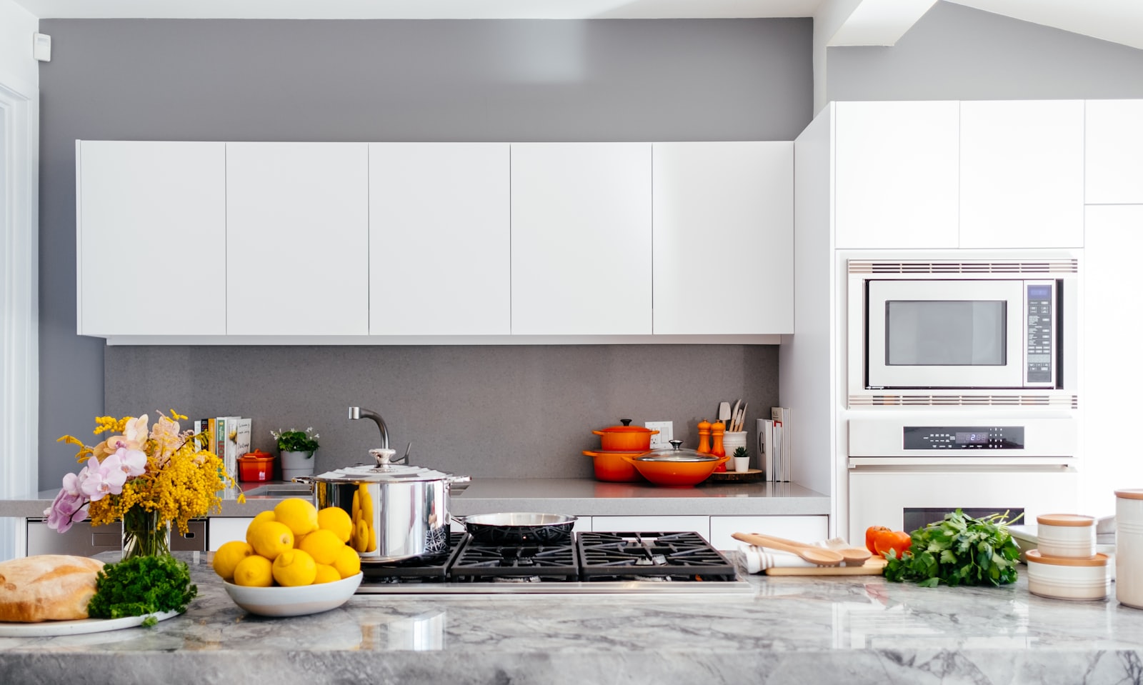 A bright, sunlit family kitchen — marble counter, a bowl of lemons, fresh flowers and a pot on the stove