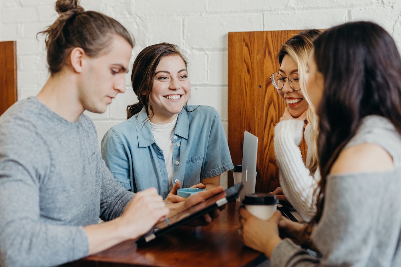 Four housemates around a table, laughing over coffee and a tablet as they sort out the week